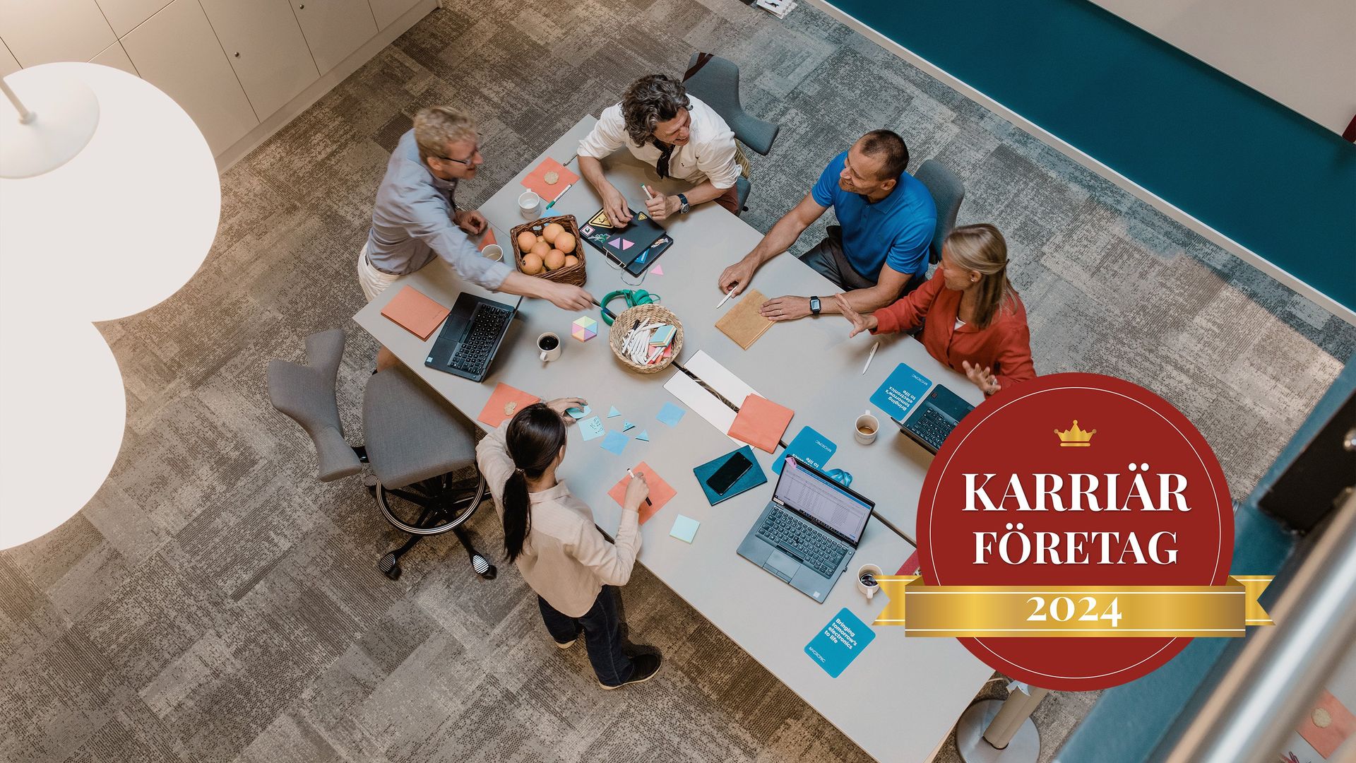 A diverse team of Mycronic employees working together at a table along with the Karriärföretagen badge