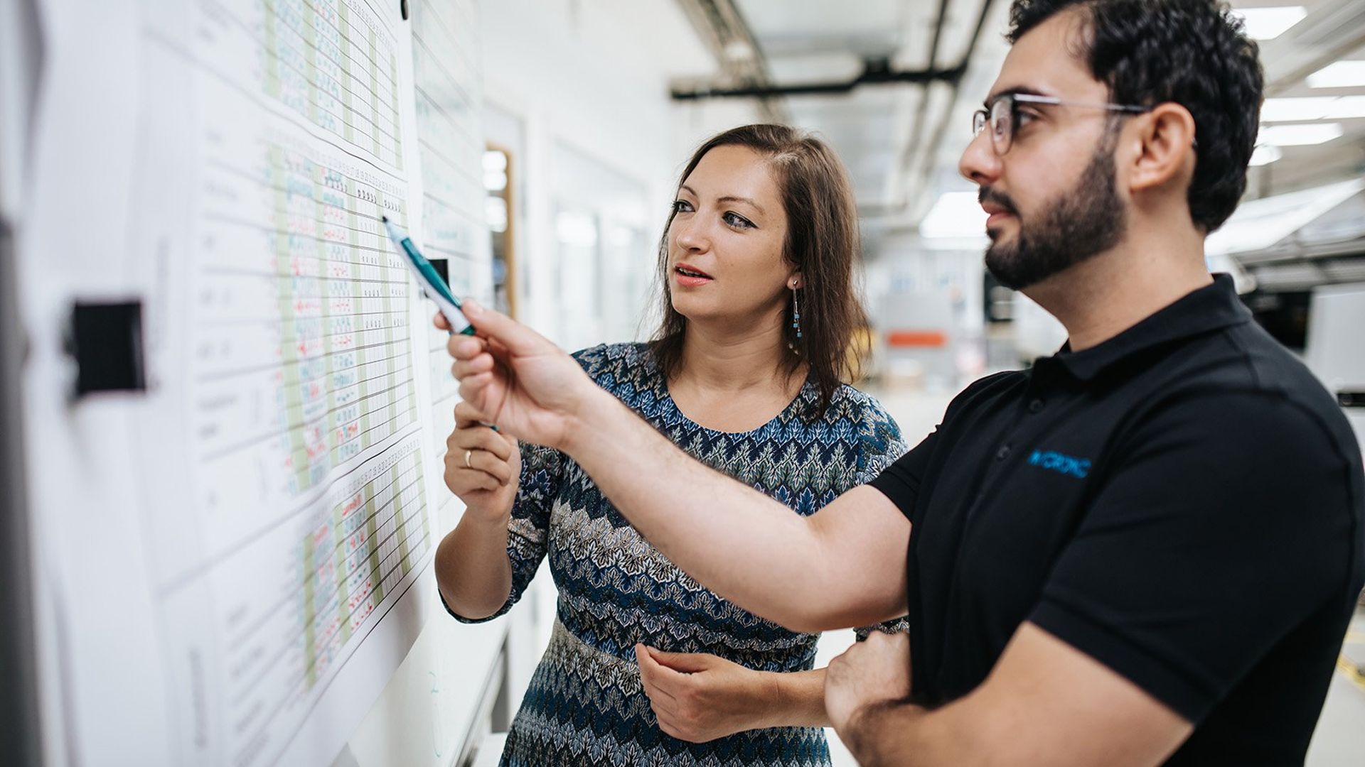 One male and one female Mycronic colleague cooperating in front of a whiteboard