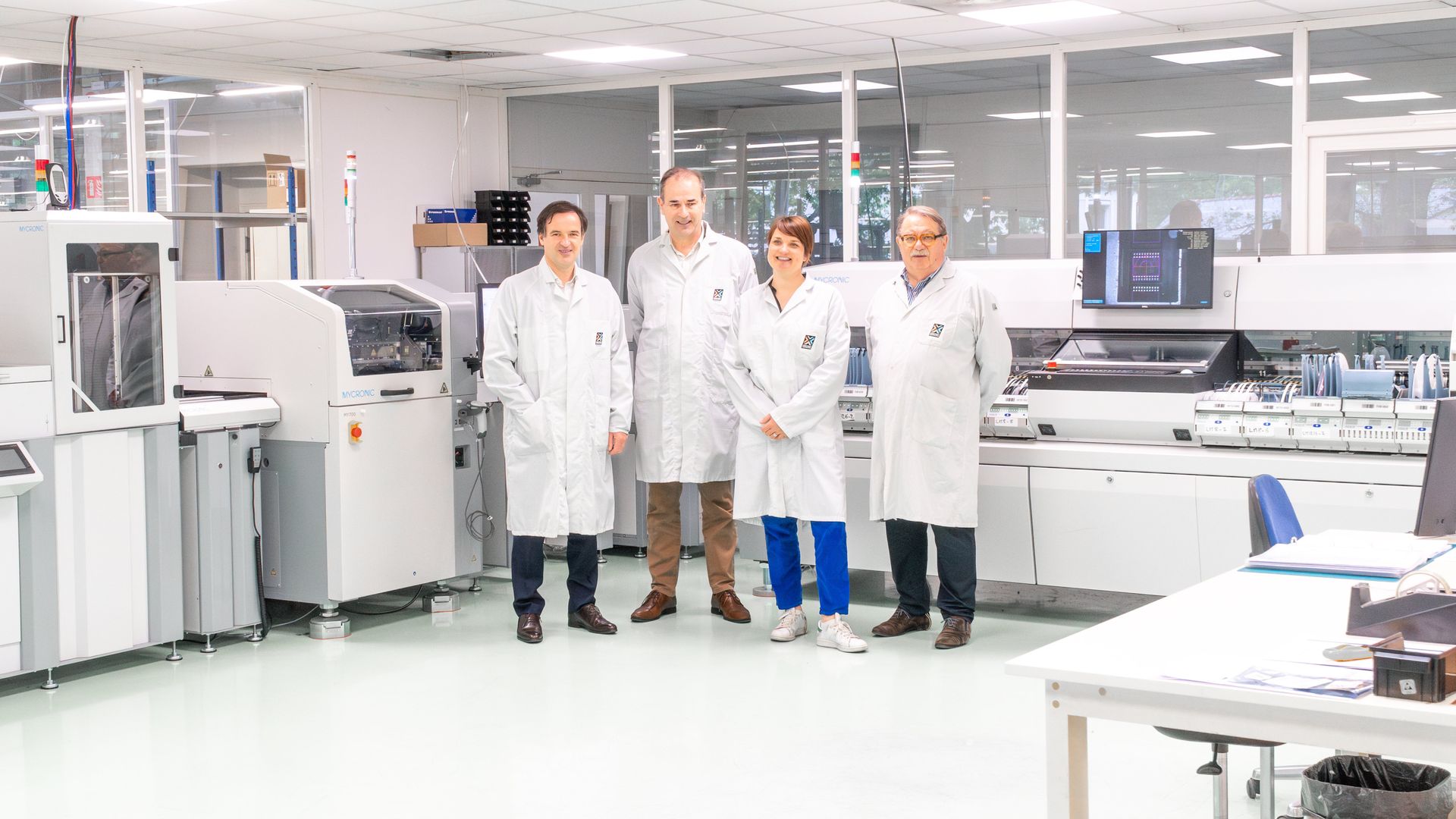 Standing in front of the new Mycronic SMT line (MY700 Jet Printer, MYPro A40DX17, 3D AOI MYPro I51, conveyors), from left to right: Cyrille Bidet (General Manager of Mycronic France), Yvon Monot (Sales Engineer Mycronic France), Solenne Grandsire (General Manager of Crossway Technologies), Michel Houdou (President of Crossway Technologies).